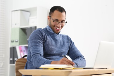 Smiling African American man writing in notebook at wooden table
