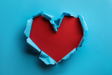 Photo of Torn heart shaped hole in light blue paper on red background