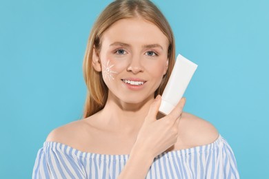 Beautiful young woman with sun protection cream on light blue background