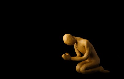 Plasticine figure of praying human on black background. Space for text
