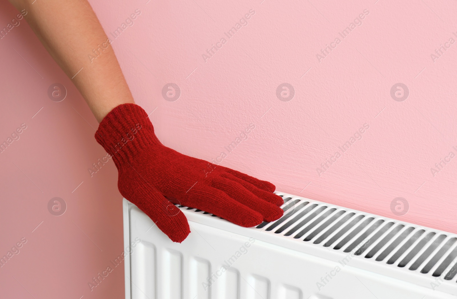 Photo of Woman in glove warming hand on heating radiator near color wall