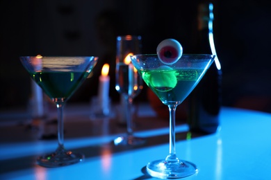Photo of Green cocktail with jelly eyeballs on table in darkness. Halloween party