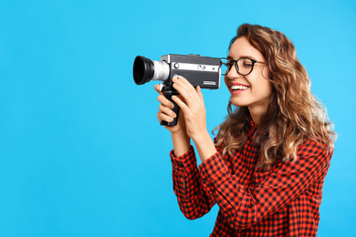 Beautiful young woman with vintage video camera on light blue background