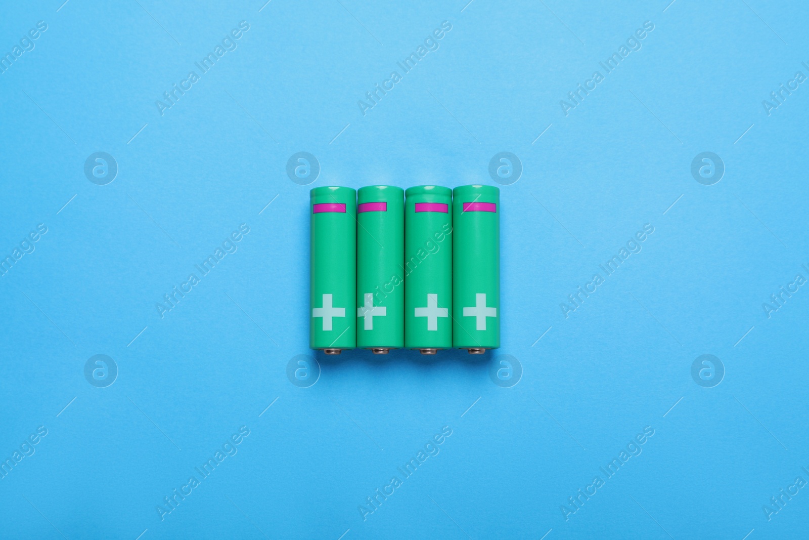 Photo of New AA size batteries on light blue background, flat lay