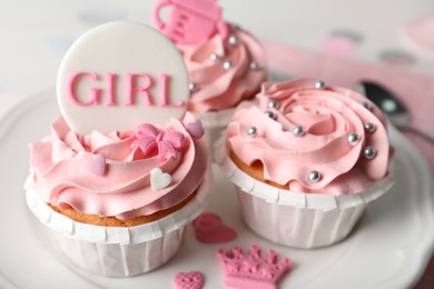 Photo of Delicious cupcakes with pink cream and toppers for baby shower on plate, closeup