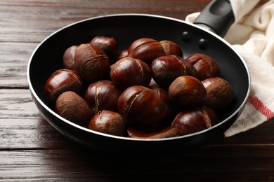 Photo of Roasted edible sweet chestnuts in frying pan on wooden table, closeup