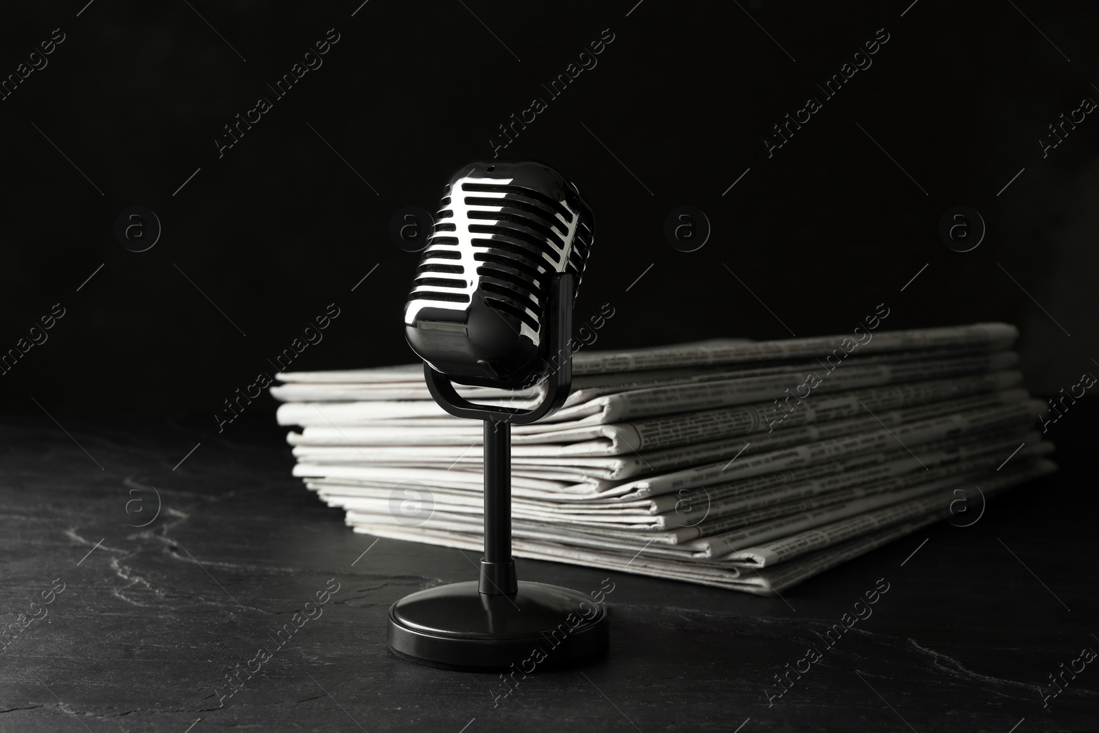 Photo of Newspapers and vintage microphone on dark stone table. Journalist's work