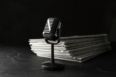 Newspapers and vintage microphone on dark stone table. Journalist's work