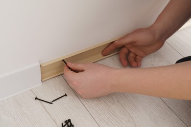 Man installing plinth on laminated floor in room, closeup