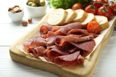 Photo of Board with delicious bresaola on white wooden table, closeup