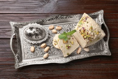Photo of Tasty halva with pistachios and mint on wooden table, top view