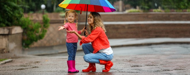 Happy mother and daughter with bright umbrella under autumn rain outdoors. Banner design