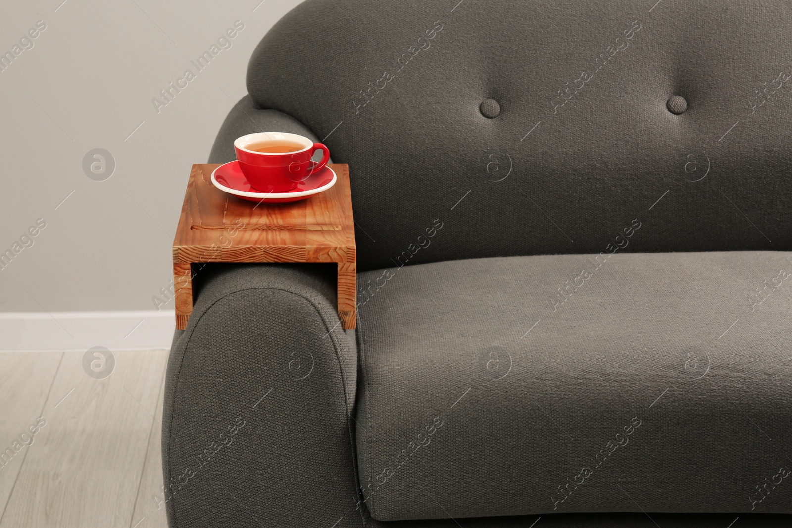 Photo of Cup of tea on sofa with wooden armrest table in room. Interior element