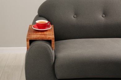 Photo of Cup of tea on sofa with wooden armrest table in room. Interior element