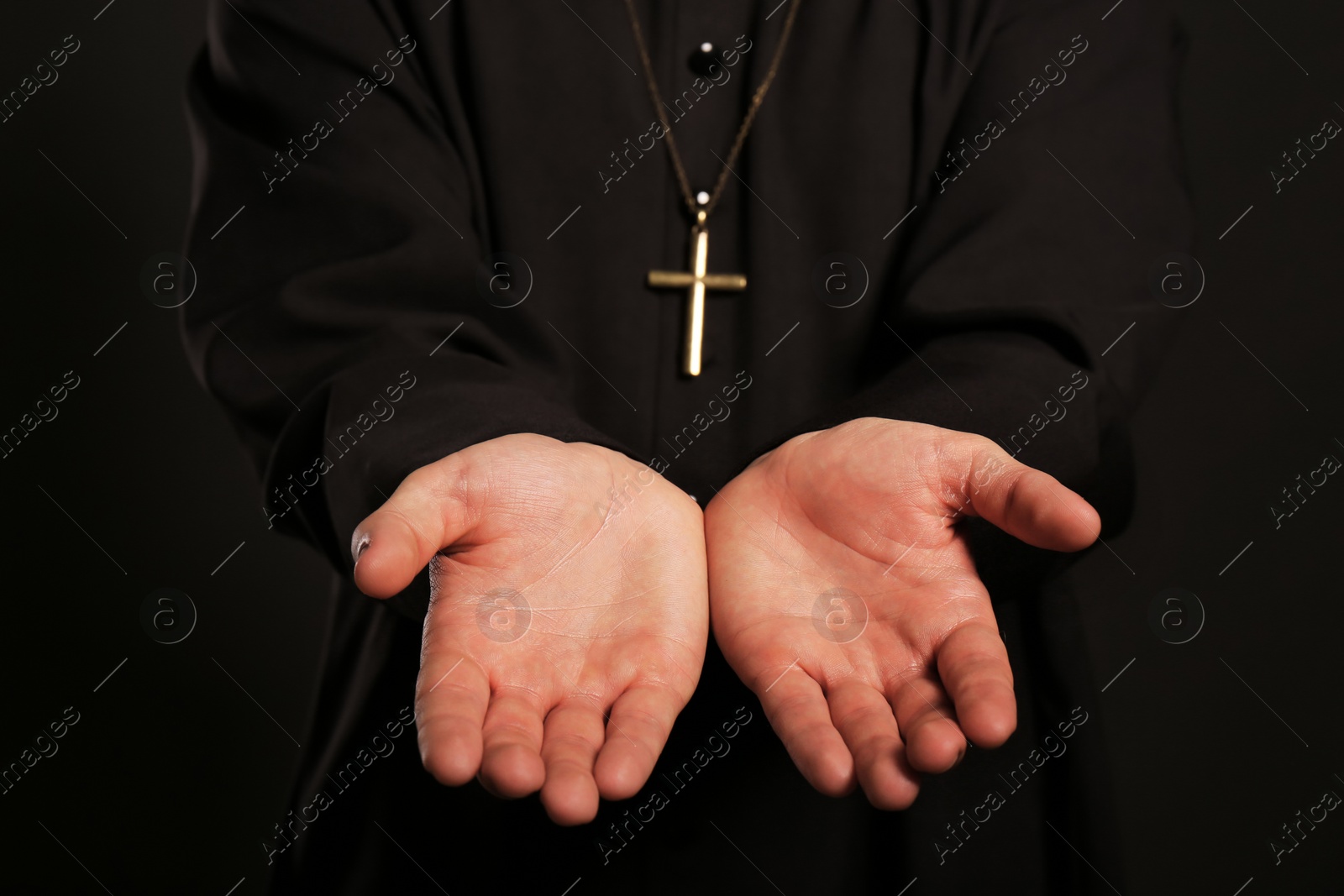 Photo of Priest reaching out his hands on black background, closeup