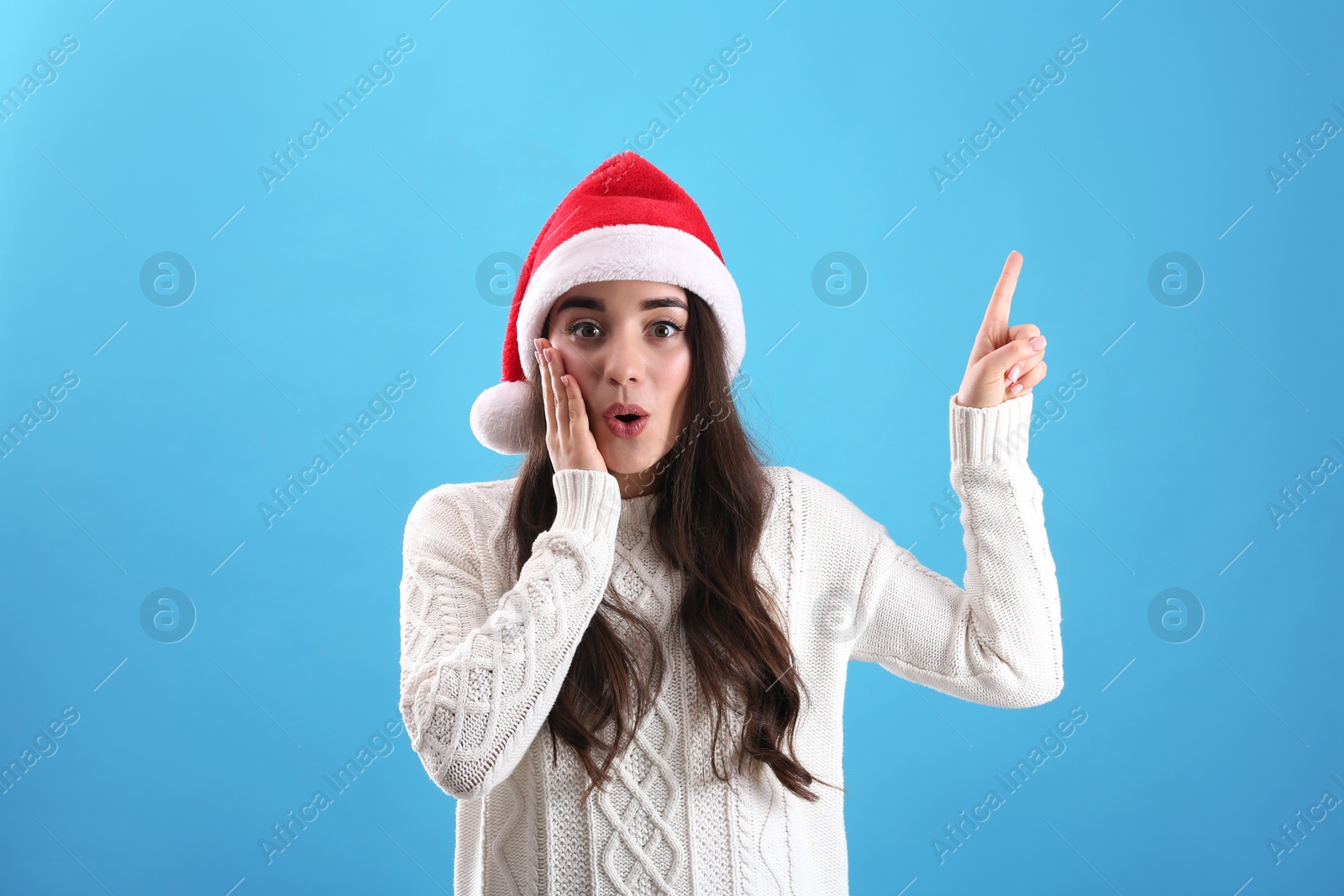 Photo of Beautiful emotional woman wearing Santa Claus hat on light blue background