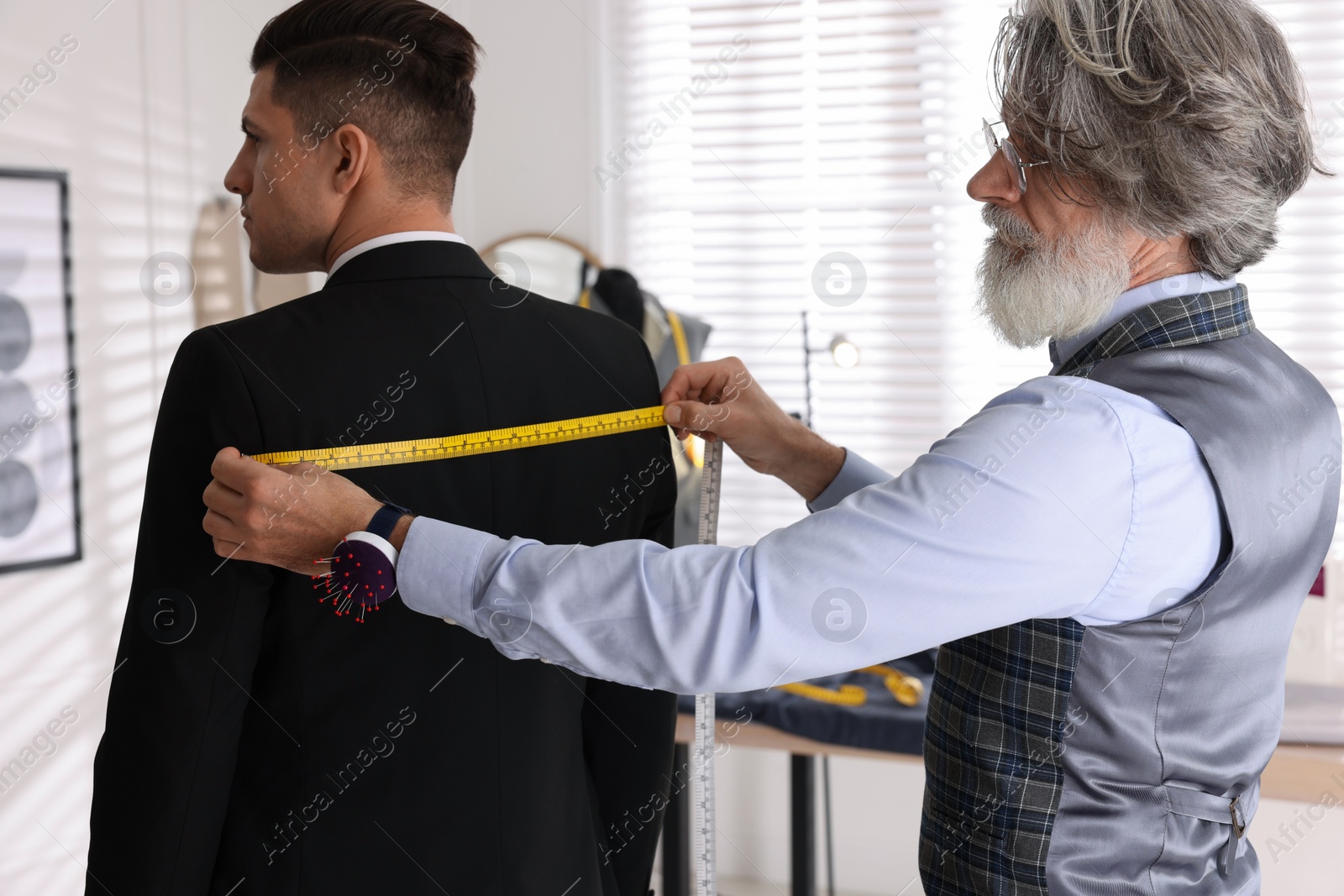 Photo of Professional tailor measuring client's back width
in atelier