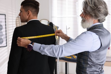 Professional tailor measuring client's back width
in atelier