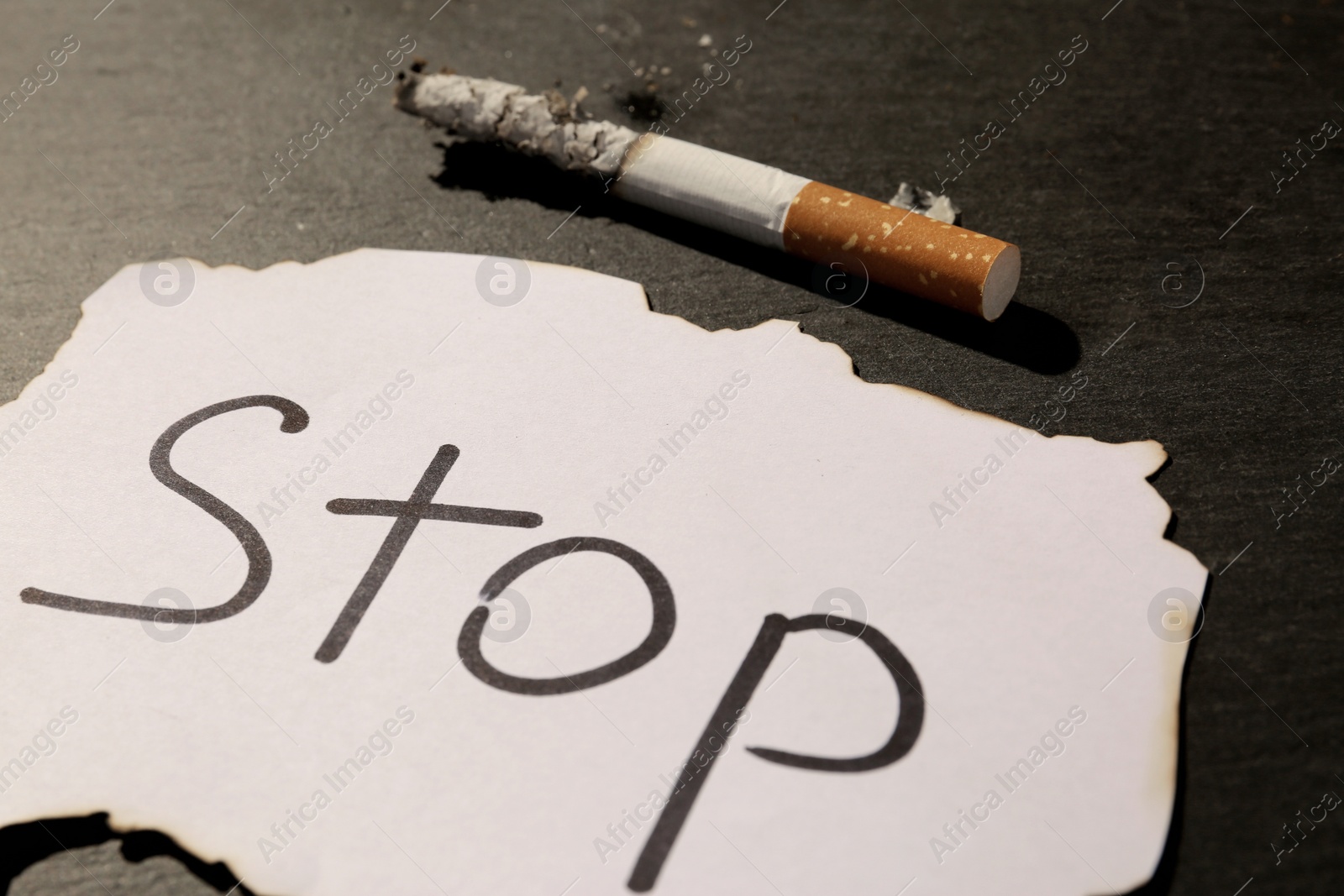 Photo of Burnt cigarette and word Stop written on paper on black table, closeup. No smoking concept