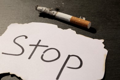 Burnt cigarette and word Stop written on paper on black table, closeup. No smoking concept