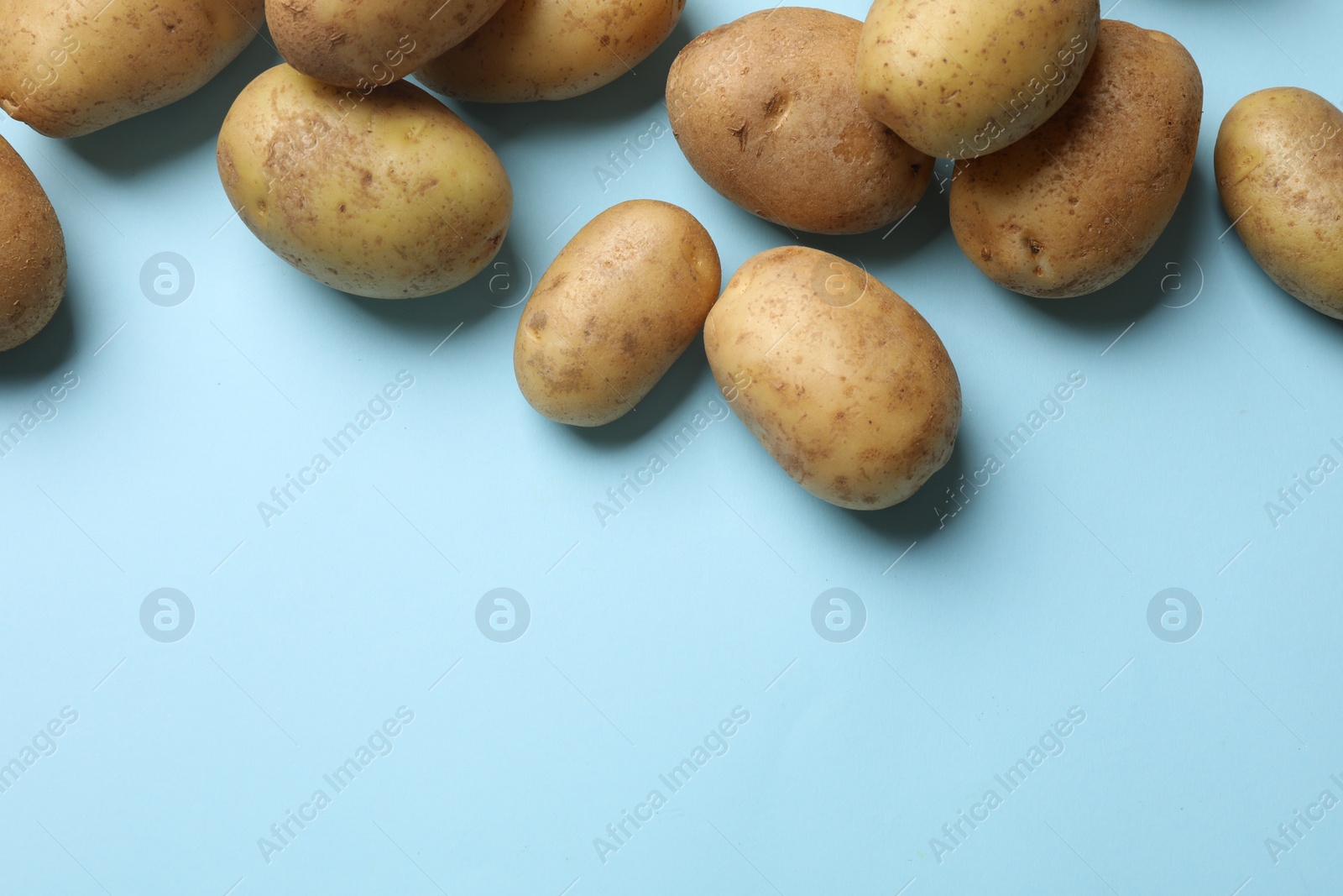 Photo of Many fresh potatoes on light blue background, flat lay. Space for text