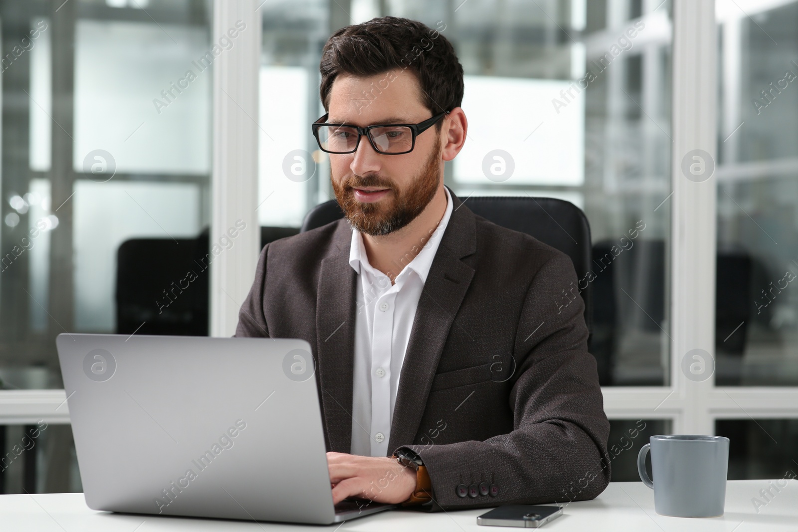 Photo of Man working on laptop at white desk in office