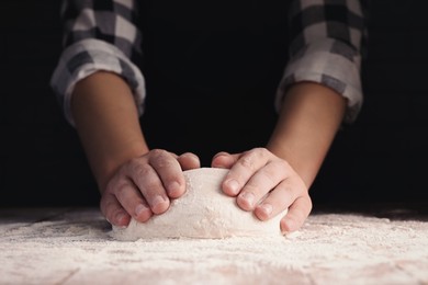 Photo of Man kneading dough at wooden table on dark background, closeup