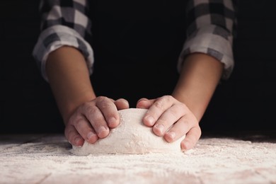 Man kneading dough at wooden table on dark background, closeup