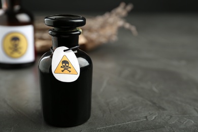 Photo of Glass bottle of poison with warning sign on grey stone table. Space for text