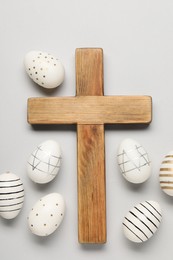 Wooden cross and painted Easter eggs on light grey background, flat lay