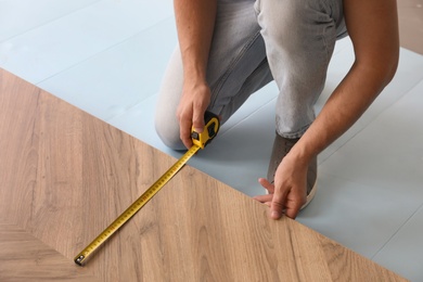 Photo of Worker installing laminated wooden floor indoors, closeup