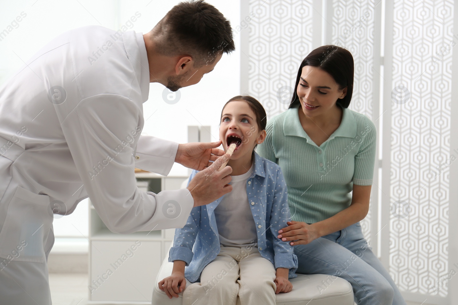 Photo of Mother with daughter visiting pediatrician in hospital. Doctor examining little girl