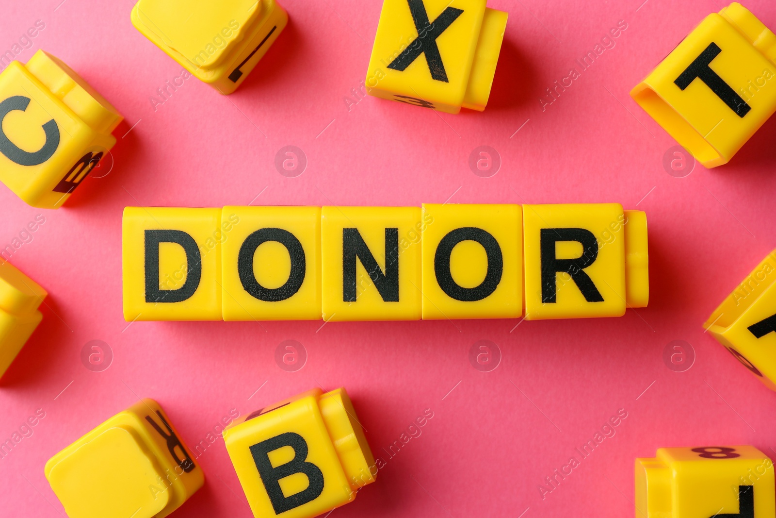 Photo of Word Donor made of yellow cubes on pink background, flat lay