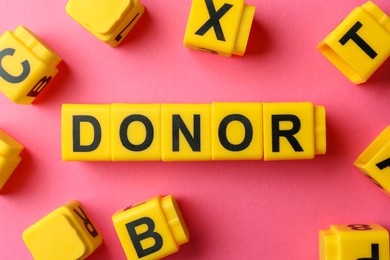 Word Donor made of yellow cubes on pink background, flat lay