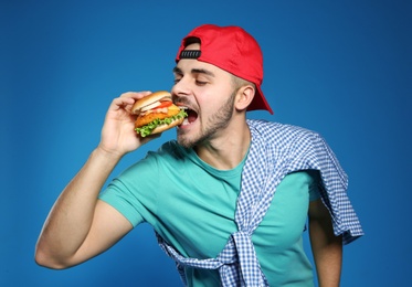 Handsome man eating tasty burger on color background