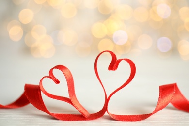 Photo of Two hearts made of red ribbon on table against blurred lights. St. Valentine's day card