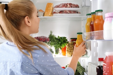 Woman taking bottle with juice out of refrigerator in kitchen