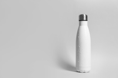 Photo of Stylish white thermo bottle with water drops on light grey background, space for text