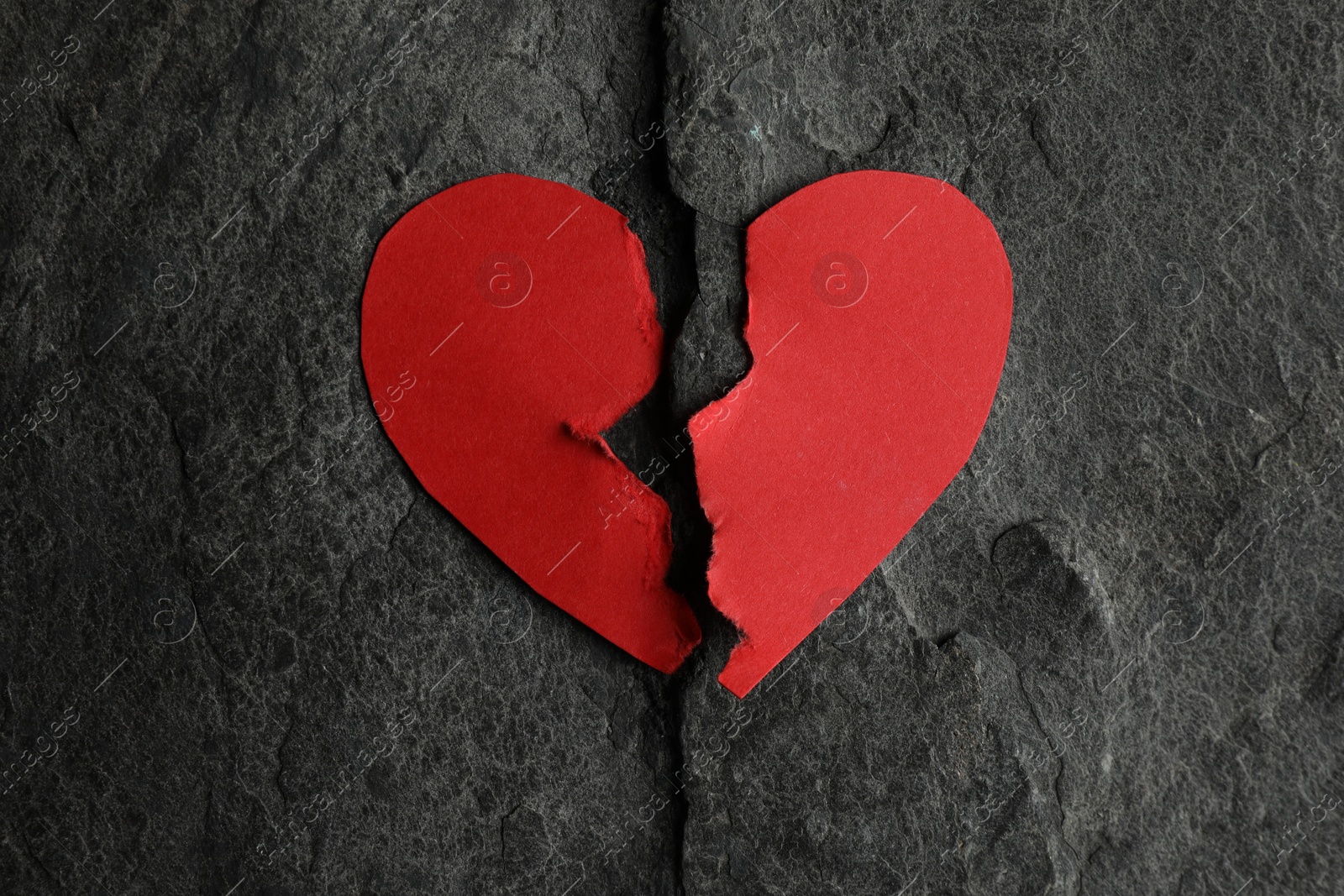 Photo of Halves of torn red paper heart on dark grey table, top view. Broken heart