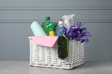 Photo of Spring cleaning. Basket with detergents, flowers and tools on grey textured table
