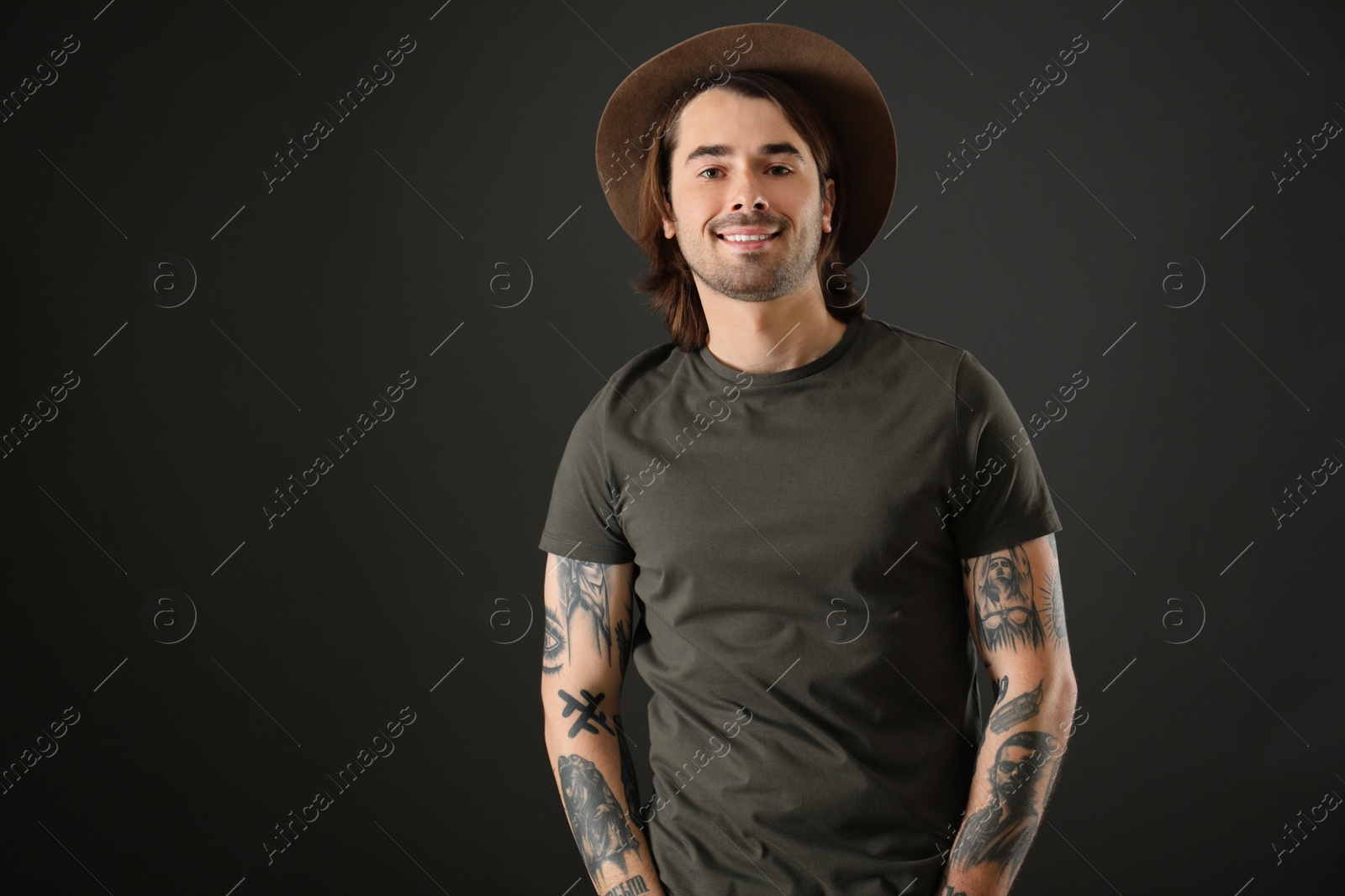 Photo of Young man with tattoos on arms against black background