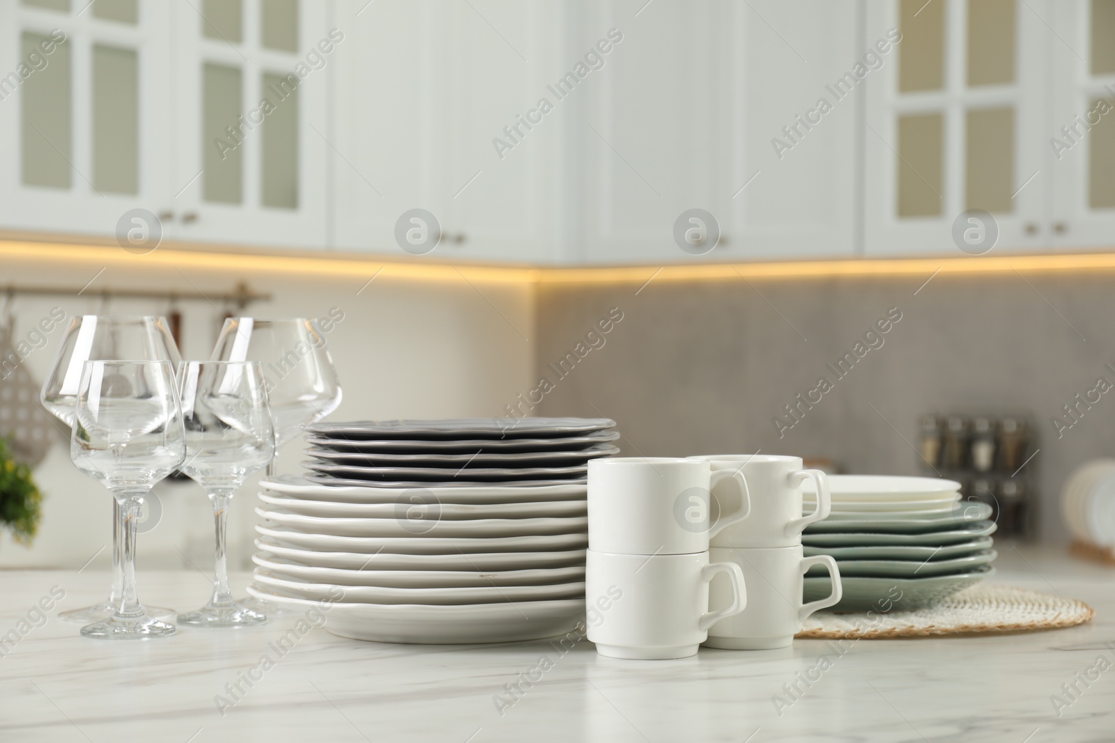 Photo of Clean plates, cups and glasses on white marble table in kitchen