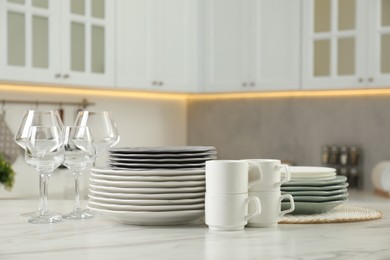 Clean plates, cups and glasses on white marble table in kitchen