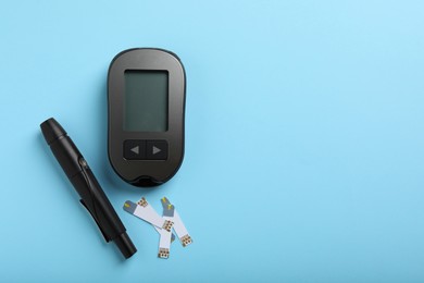 Digital glucometer, lancet pen and test strips on light blue background, flat lay with space for text. Diabetes control