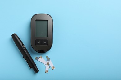 Photo of Digital glucometer, lancet pen and test strips on light blue background, flat lay with space for text. Diabetes control