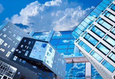 Image of Beautiful blue sky with clouds reflecting in windows of modern buildings. Low angle view