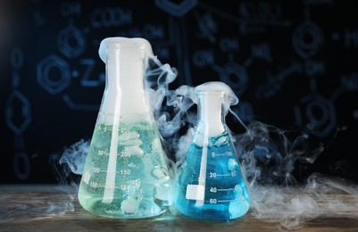 Laboratory glassware with colorful liquids and steam on wooden table against black background. Chemical reaction
