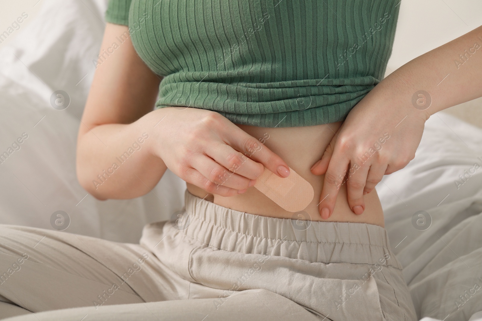 Photo of Woman applying contraceptive patch onto her belly on bed, closeup