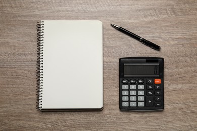 Calculator and office stationery on wooden table, flat lay. Space for text