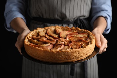 Woman holding plate with delicious apple pie on black background, closeup